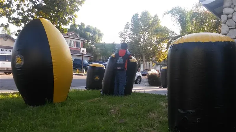 Black and gold inflatable laser tag bunkers set up on a front lawn, with a player in a tactical vest taking cover